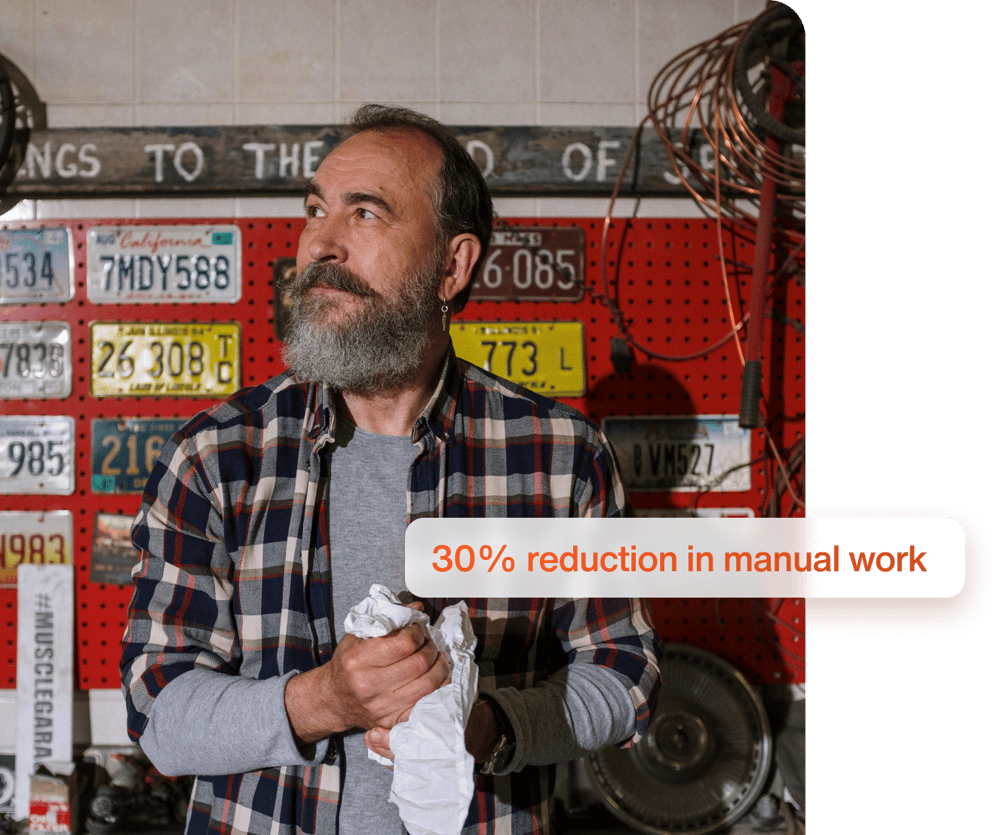 Man med skägg i en verkstad, omgiven av registreringsskyltar, med texten '30% reduction in manual work