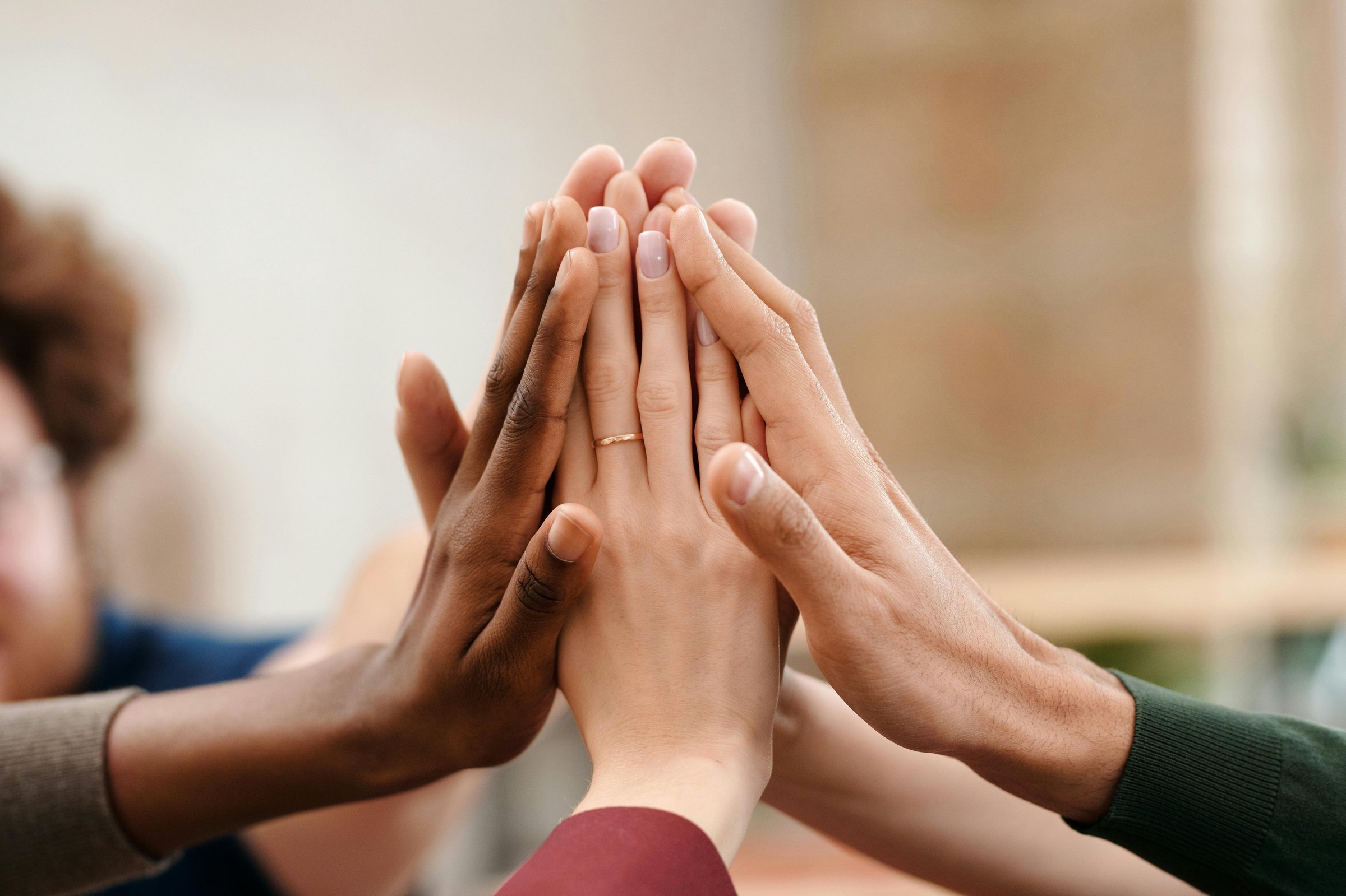 Flera händer i olika hudtoner möts i en gemensam high-five, symboliserar samarbete, gemenskap och mångfald