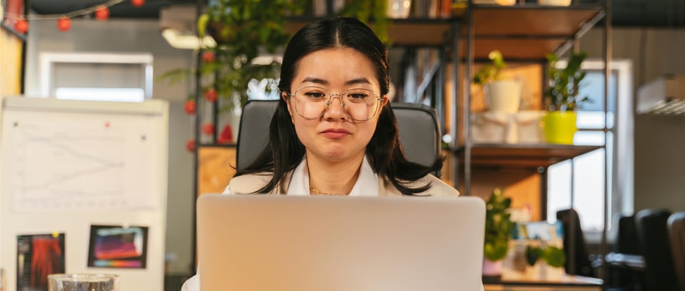 kvinna med mörkt hår och glasögon sitter framför en laptop