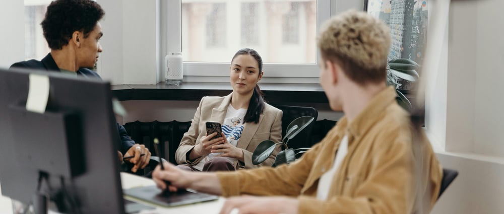 Två manliga och en kvinnlig kollega sitter i kontorsmiljö och har en konversation