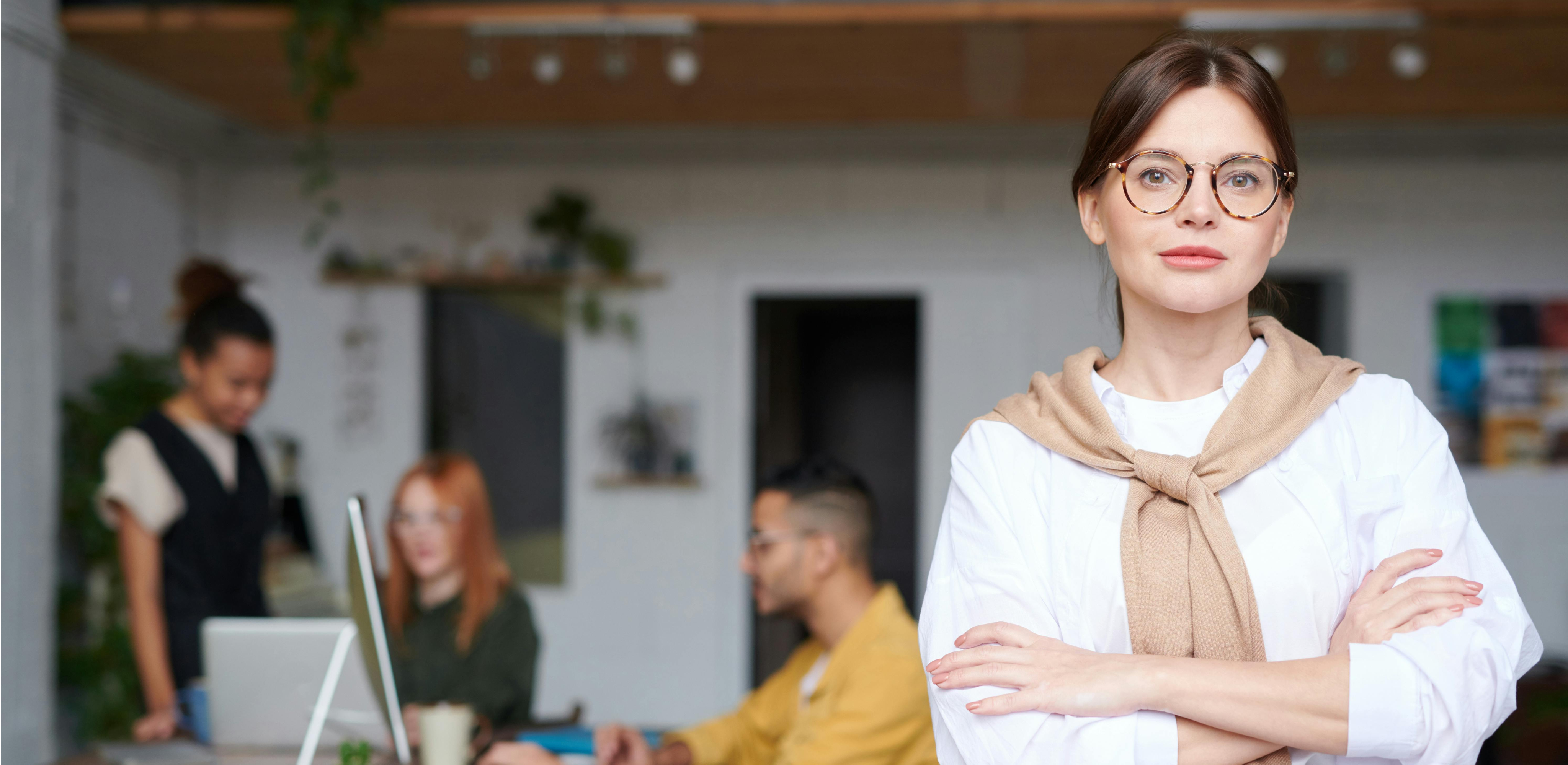 Kvinna står med armarna i kors och kollar in i kameran i kontorsmiljö