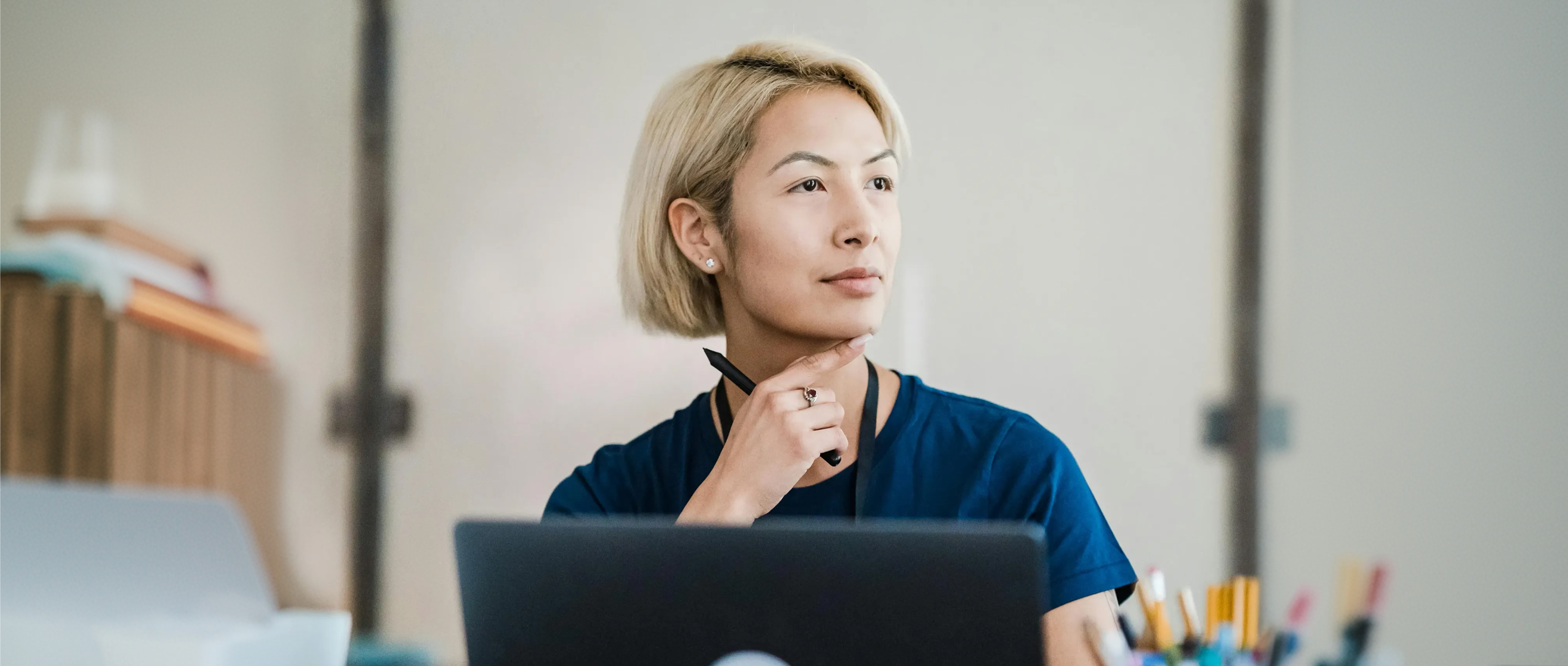 kvinna med blont hår sitter framför en laptop och tittar upp på något som finns längre bort